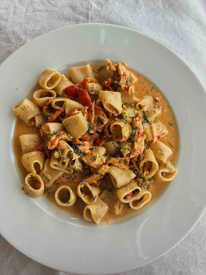 Northern Pasta Co. rigatoni served in a creamy sauce with salmon, tomatoes, and fresh herbs on a white plate.