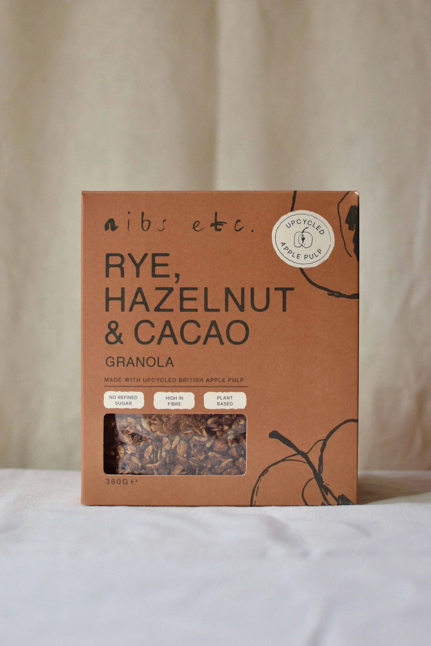 Nibs Etc. rye, hazelnut and cacao granola in sustainable brown cardboard packaging with apple pulp detail