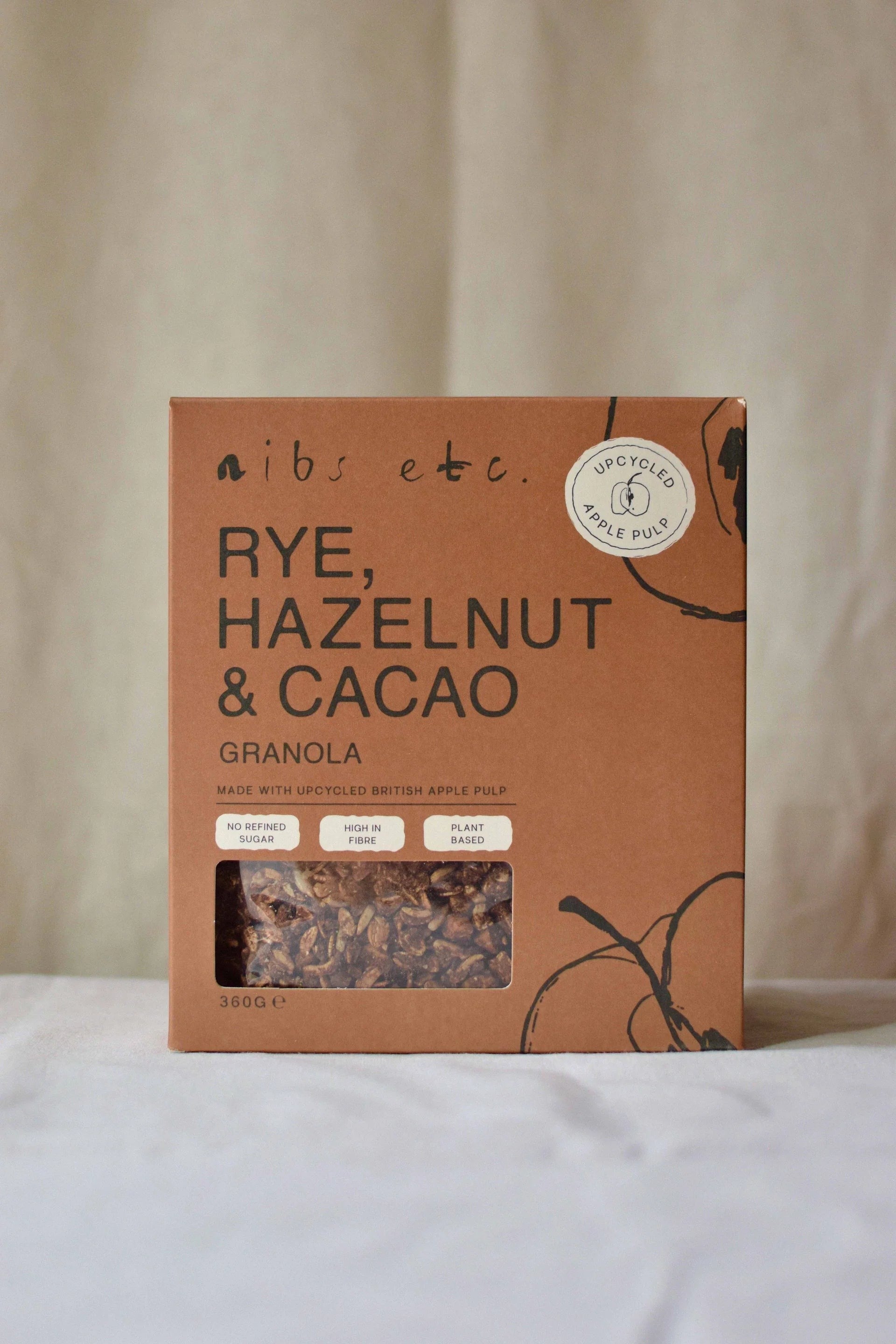 Nibs Etc. rye, hazelnut and cacao granola in sustainable brown cardboard packaging with apple pulp detail