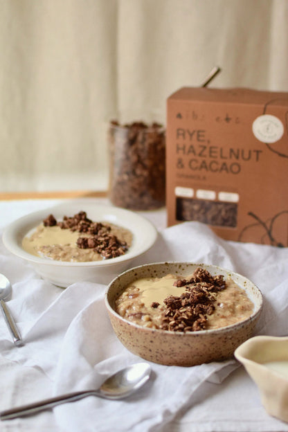 Nibs Etc. rye, hazelnut, and cacao granola served in speckled bowls with a branded box in the background.