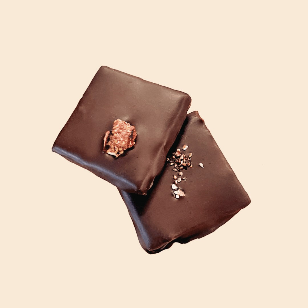 Two Cosmic Dealer dark chocolate squares topped with fig and sea salt against a light cream background