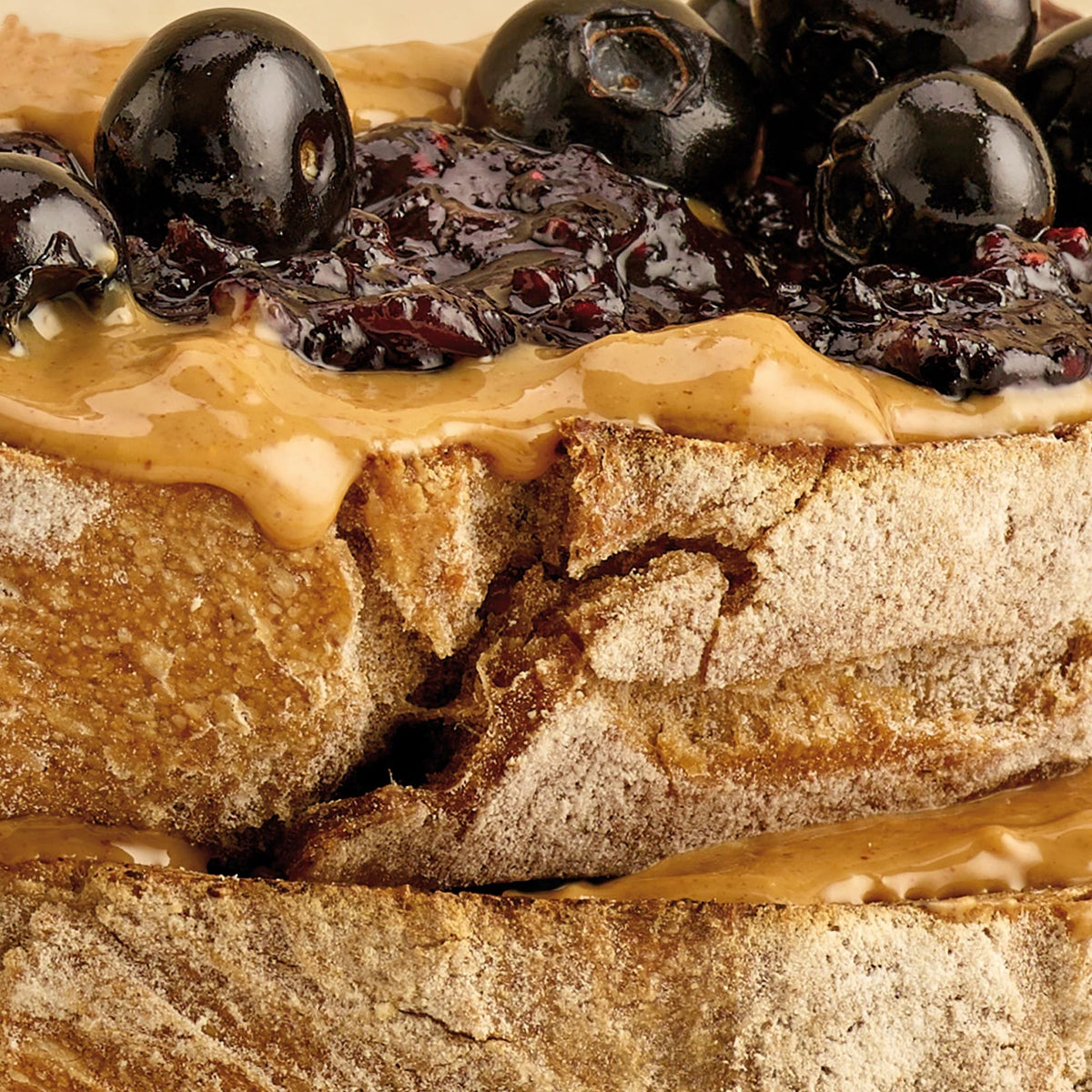 Pip & Nut smooth peanut butter spread on toasted sourdough bread topped with dark berry jam and fresh blueberries