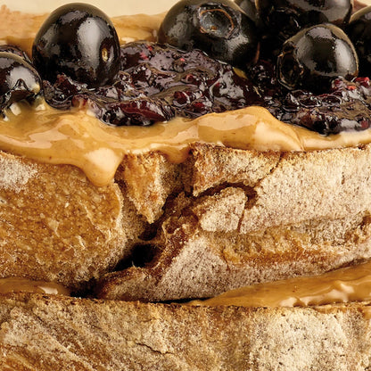 Pip & Nut smooth peanut butter spread on toasted sourdough bread topped with dark berry jam and fresh blueberries