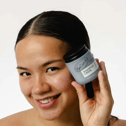 UpCircle model holding a jar of UpCircle Refillable Shampoo Crème with pink berry extracts against a white background