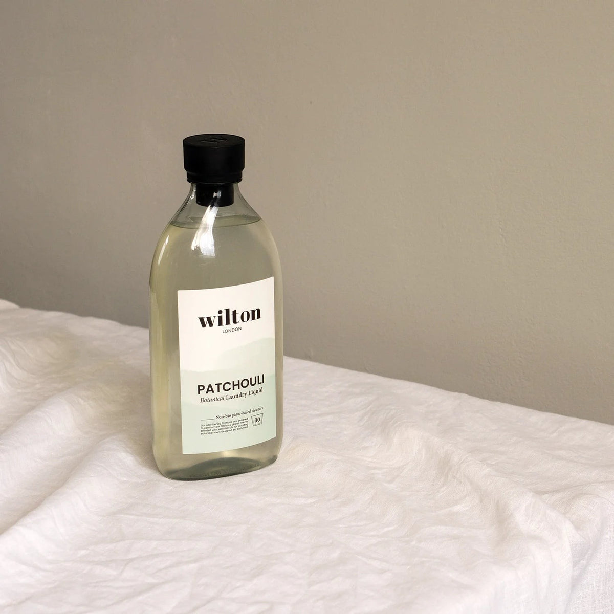 Wilton London Patchouli non-bio laundry liquid in a clear 1.05L bottle on a white linen surface.