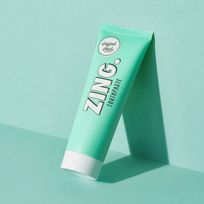 Zing vegan mint enamel whitening toothpaste in a light green tube against a matching studio background