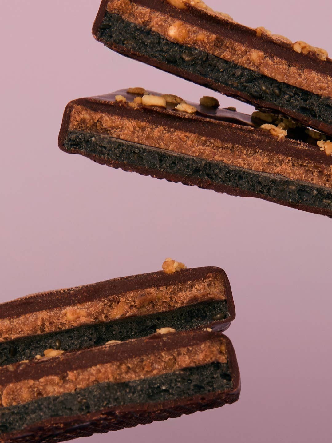 Cosmic Dealer chocolate squares with layered peanut butter, tahini, and chai spice on a soft pink background.