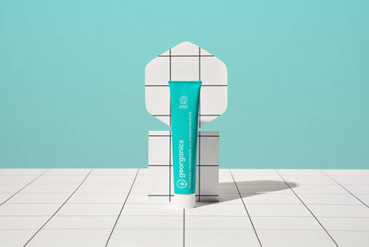 georganics fresh mint toothpaste tube with hydroxyapatite and fluoride on a white grid display against a teal background