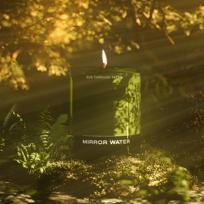 Mirror Water Sun Through Trees soy wax candle in a green glass jar, glowing in a sunlit forest setting with ferns.