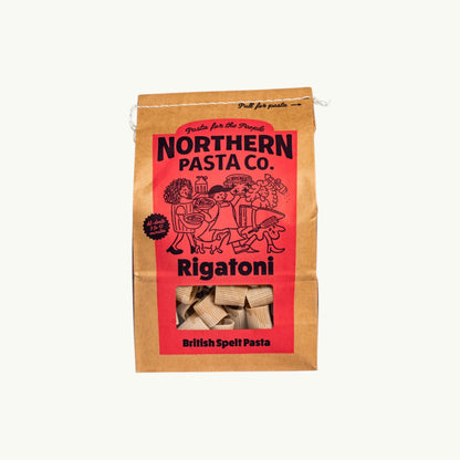 Northern Pasta Co. Rigatoni in a brown paper bag with red branding and a window showing the spelt pasta shapes.