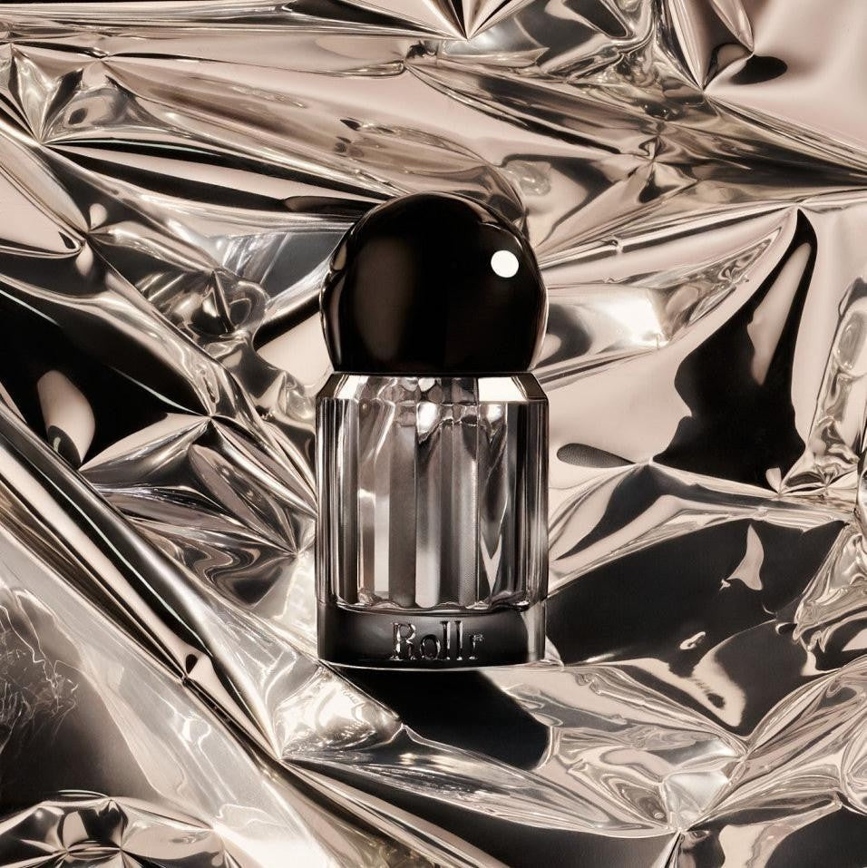 Rollr refillable glass roll-on deodorant bottle with a black cap set against a reflective silver foil background