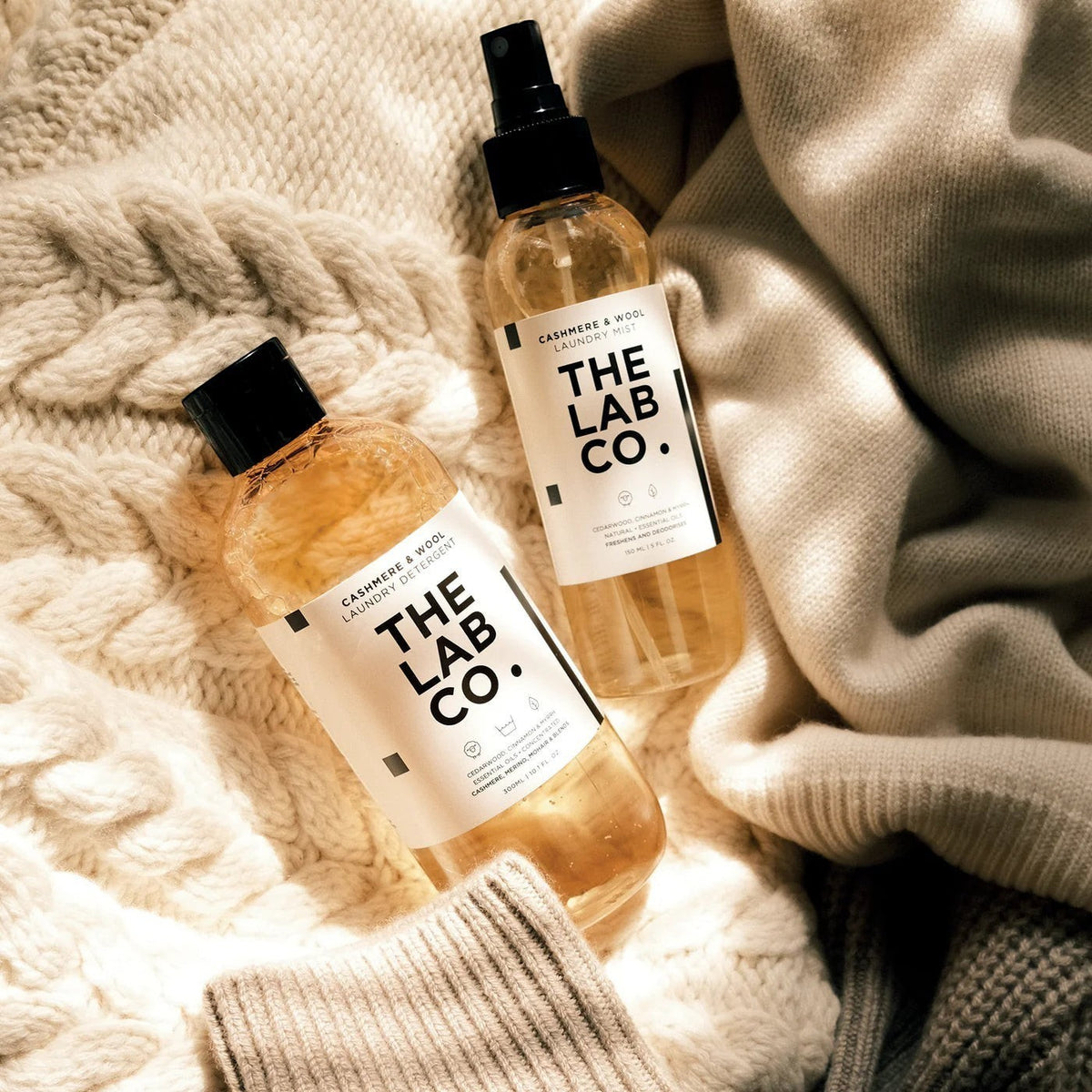 The Lab Co Cashmere and Wool laundry detergent and mist bottles resting on a soft cream-colored knitted wool sweater.