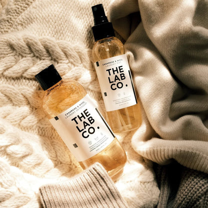 The Lab Co Cashmere and Wool laundry detergent and mist bottles resting on a soft cream-colored knitted wool sweater.
