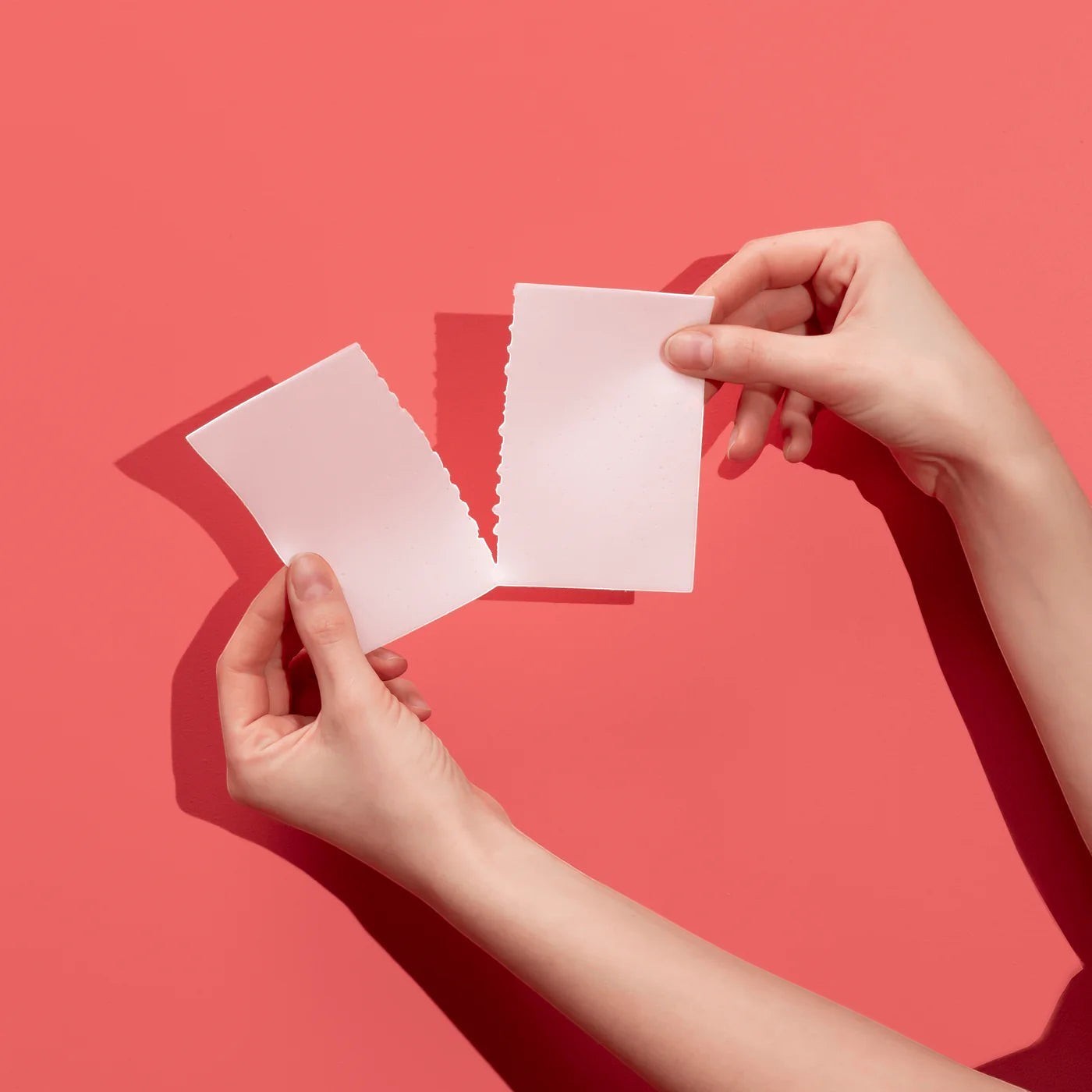 The Lab Co hands tearing a white laundry detergent strip against a vibrant coral pink background
