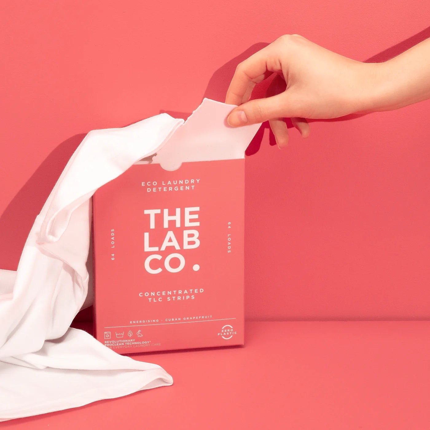 The Lab Co. energising laundry detergent strips in pink plastic-free packaging held by a hand