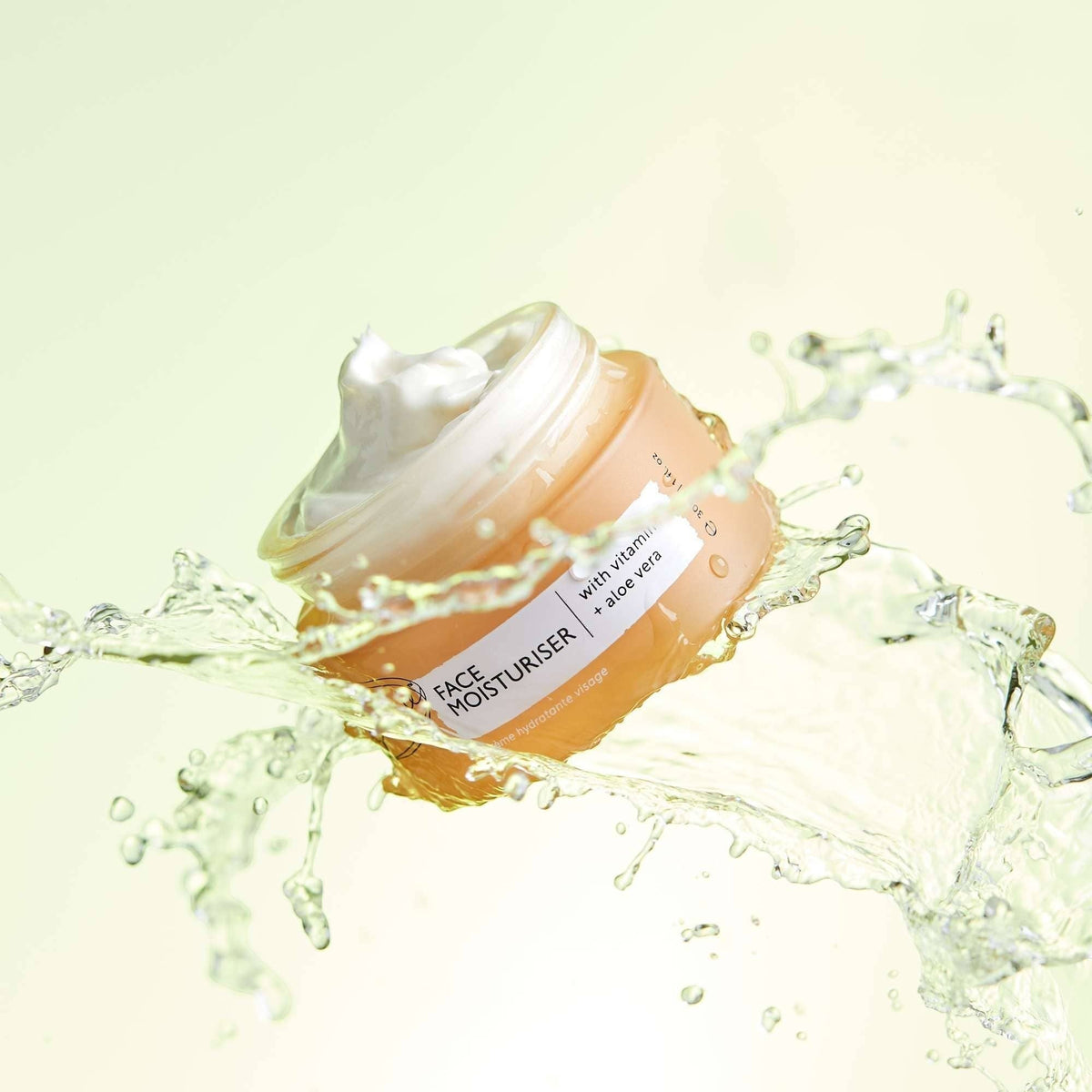 upcircle face moisturiser in a glass jar surrounded by a refreshing water splash on a soft green background.