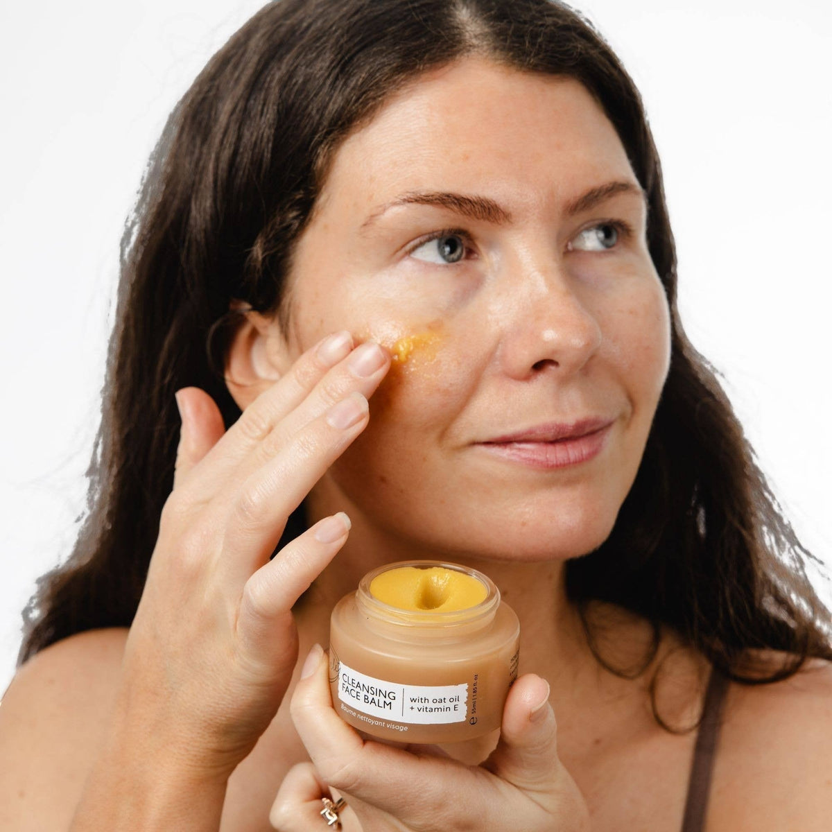 upcircle natural cleansing balm being applied to face by a woman holding the 55ml jar with oat and sea buckthorn oils