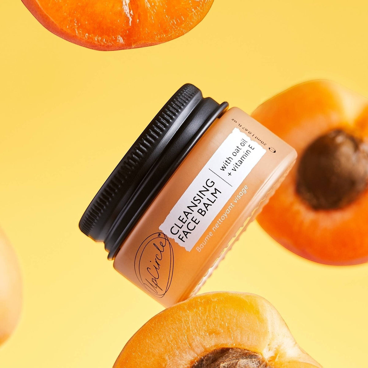 upcircle natural cleansing balm in a jar surrounded by fresh apricot halves against a bright yellow background.