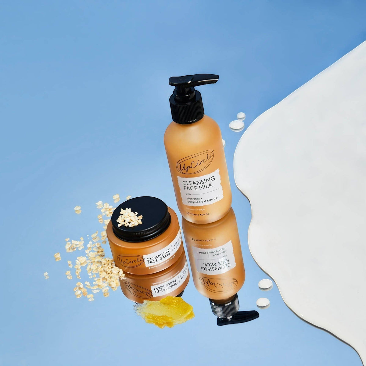 upcircle natural cleansing balm and face milk set with oat powder on a reflective blue surface