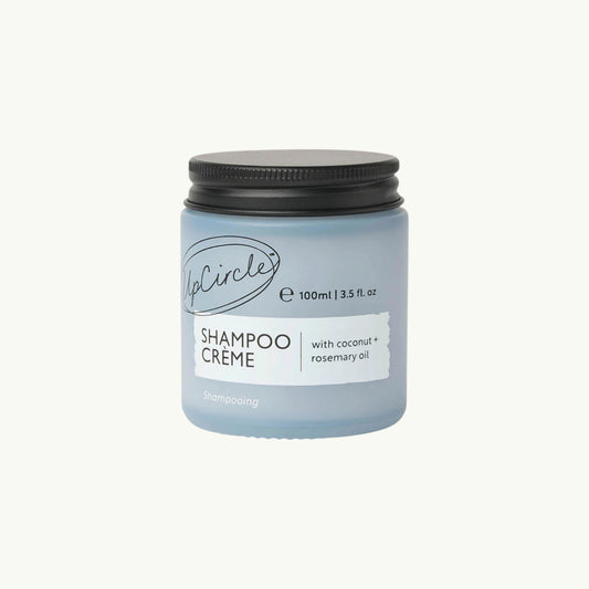 BRiMM UpCircle refillable shampoo crème in a frosted blue glass jar with a black lid, featuring coconut and rosemary.